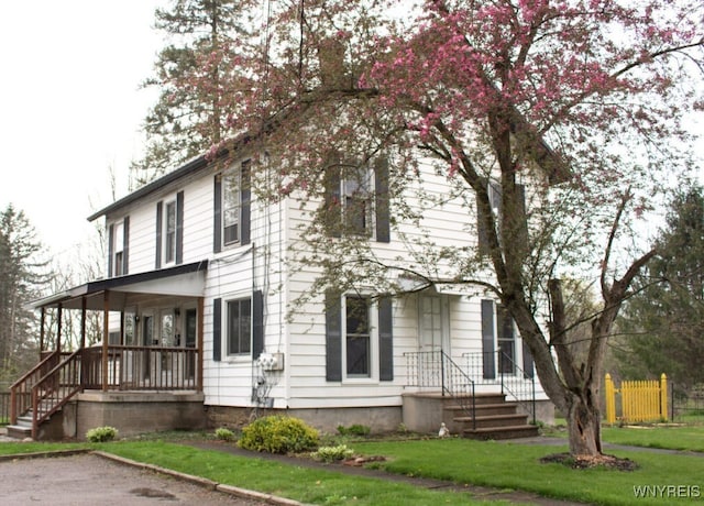 view of front of home featuring covered porch, fence, and a front lawn