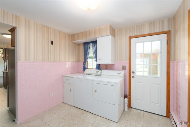washroom with washing machine and clothes dryer, baseboard heating, wainscoting, cabinet space, and wallpapered walls