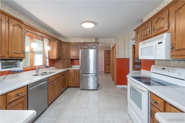 kitchen featuring appliances with stainless steel finishes, brown cabinets, a sink, light countertops, and wallpapered walls