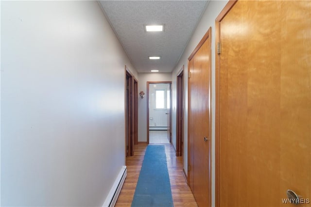 hall featuring a textured ceiling, a baseboard heating unit, baseboards, and light wood-type flooring