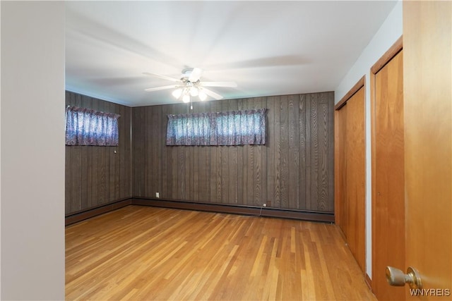 unfurnished room with wooden walls, baseboard heating, ceiling fan, and wood finished floors