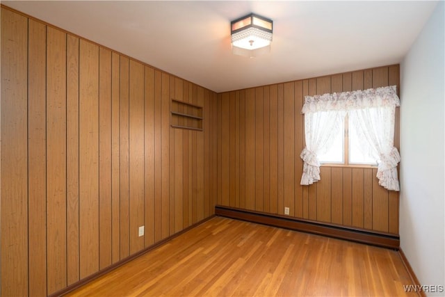 empty room featuring wooden walls, light wood-style floors, and a baseboard radiator
