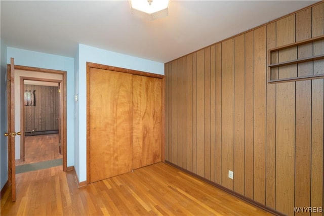 unfurnished bedroom with a closet, baseboards, wooden walls, a baseboard heating unit, and light wood-style flooring