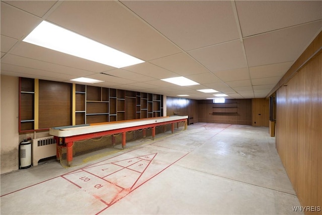 finished basement featuring wooden walls, radiator, and a paneled ceiling