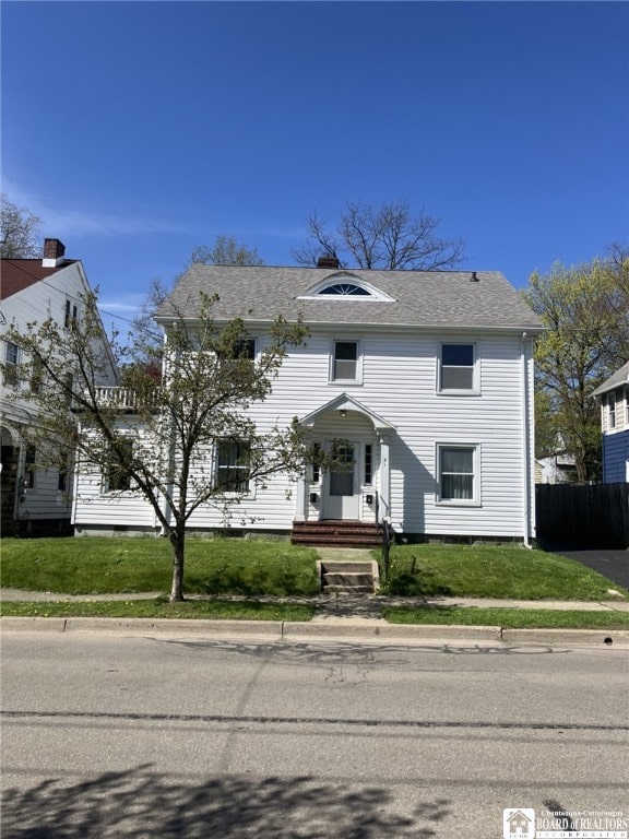 colonial house with fence, roof with shingles, and a front yard