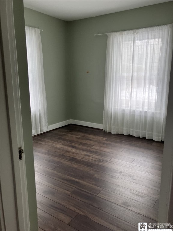 spare room with baseboards and dark wood-style flooring