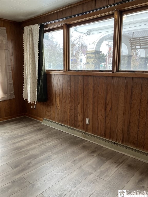 spare room with light wood-type flooring, wood walls, and baseboard heating