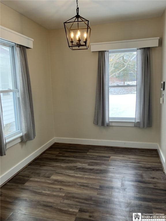unfurnished room with baseboards, a chandelier, and dark wood finished floors