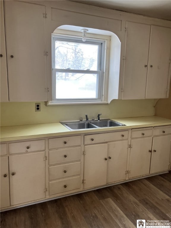 kitchen with arched walkways, a sink, light countertops, white cabinets, and dark wood-style floors