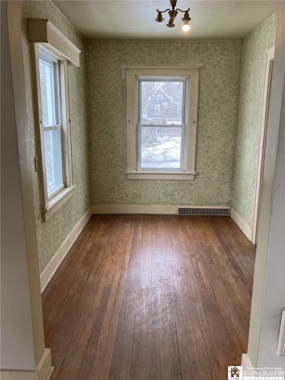 empty room featuring baseboards, a notable chandelier, hardwood / wood-style flooring, and visible vents