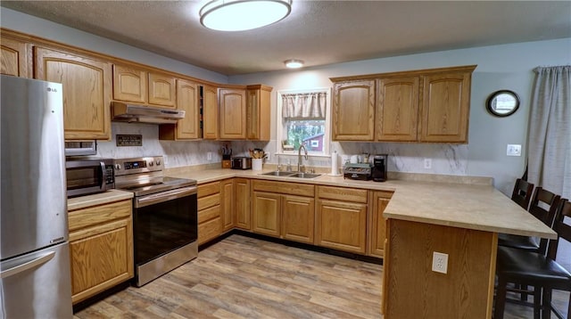 kitchen with a sink, a breakfast bar area, stainless steel appliances, a peninsula, and under cabinet range hood