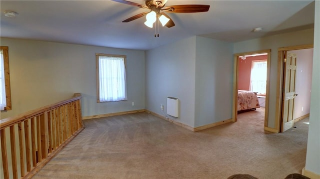 empty room featuring heating unit, baseboards, ceiling fan, and light carpet