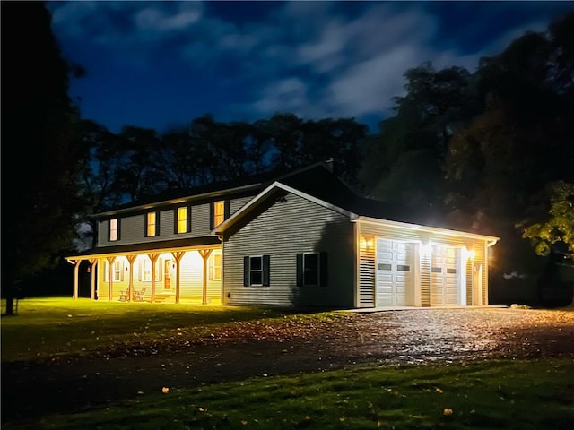 view of front of house featuring an attached garage, dirt driveway, a lawn, and covered porch