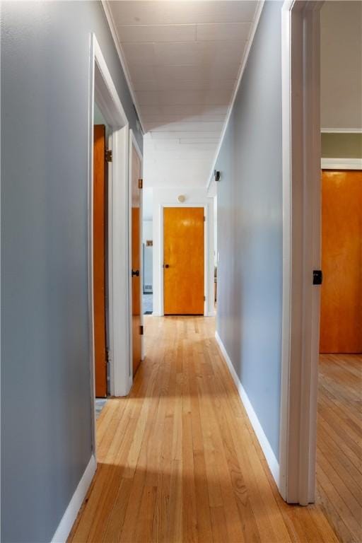 hallway with light wood-style floors, baseboards, and ornamental molding