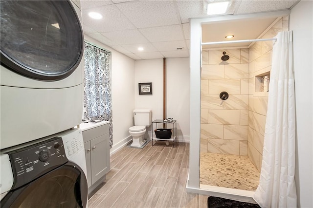 full bath featuring toilet, stacked washing maching and dryer, a tile shower, and wood tiled floor
