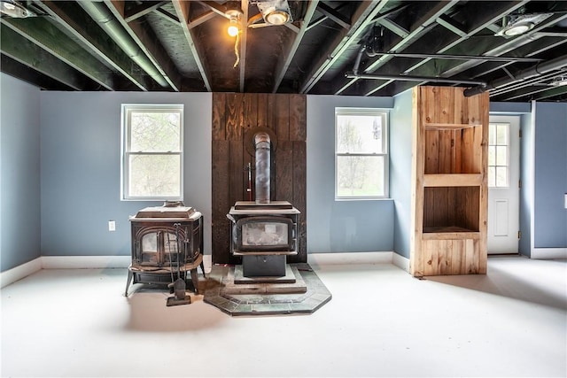 sitting room featuring baseboards, a wood stove, and concrete flooring