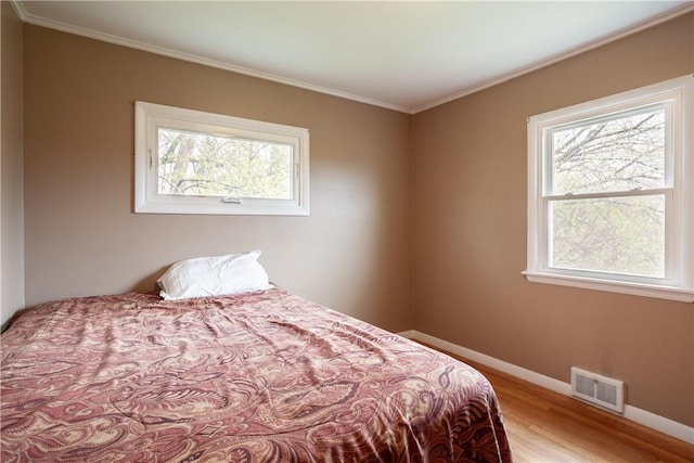 bedroom featuring visible vents, baseboards, crown molding, and wood finished floors