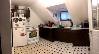 kitchen with white appliances, dark brown cabinetry, lofted ceiling, and light countertops