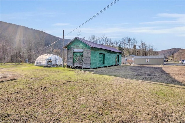 view of front of home with an outdoor structure, a mountain view, a greenhouse, and a front yard