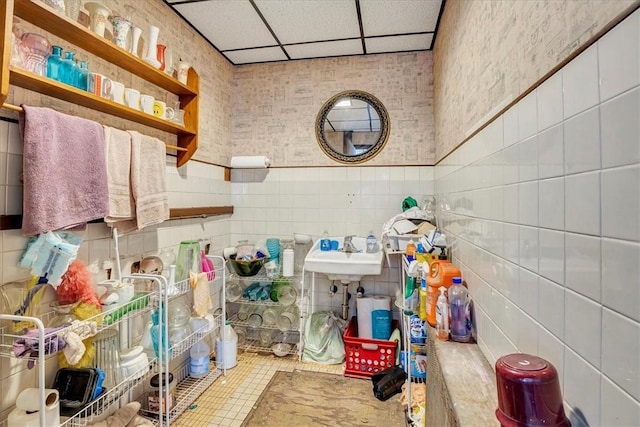 bathroom with a sink, a paneled ceiling, tile patterned floors, and tile walls