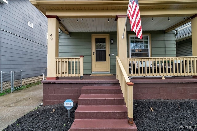 view of exterior entry with fence and covered porch