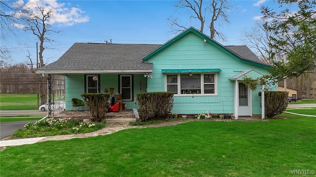 view of front of house with roof with shingles, covered porch, and a front yard