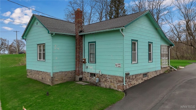 view of side of home with roof with shingles, a chimney, and a yard