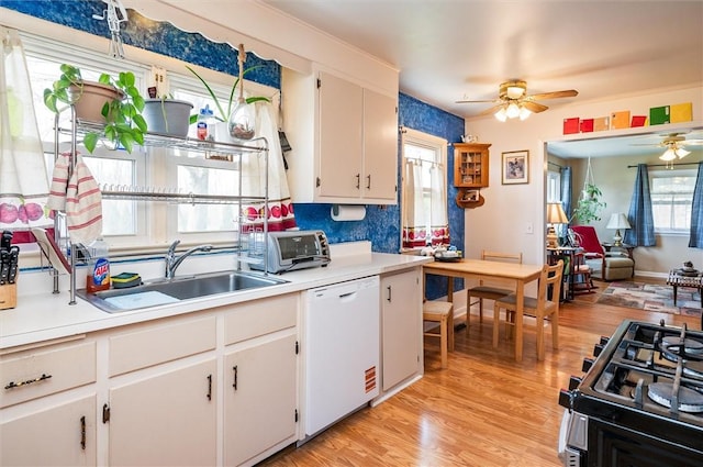 kitchen with a ceiling fan, white dishwasher, gas range oven, light countertops, and a sink