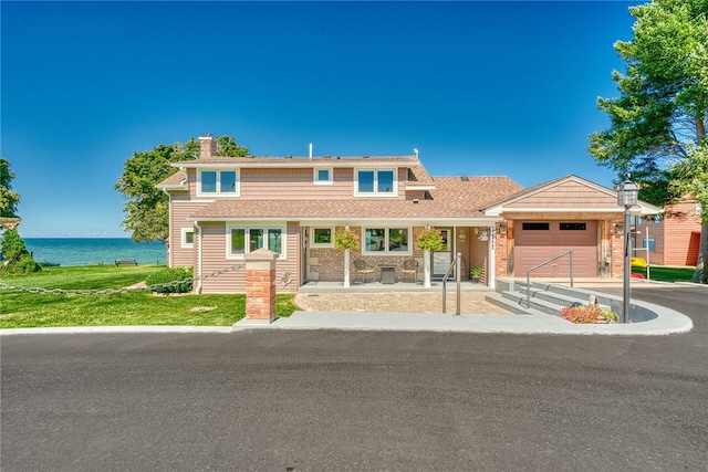 view of front of home featuring a shingled roof, a garage, a porch, a chimney, and a water view