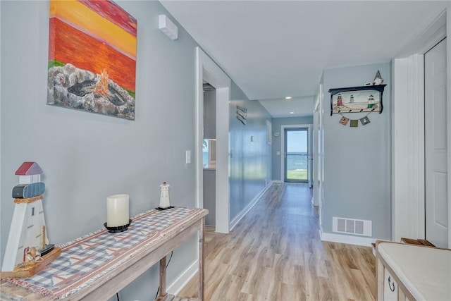 hall featuring baseboards, light wood-style flooring, and visible vents