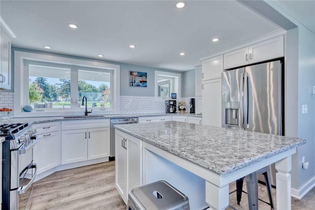 kitchen featuring appliances with stainless steel finishes, light stone countertops, a sink, light wood-style floors, and white cabinetry