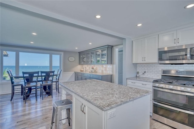 kitchen featuring decorative backsplash, appliances with stainless steel finishes, a center island, white cabinetry, and light wood-style flooring