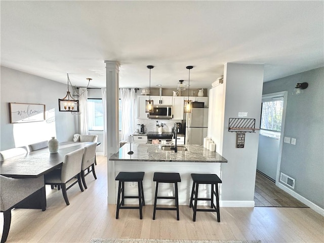 kitchen featuring white cabinets, a breakfast bar, a sink, stainless steel appliances, and visible vents