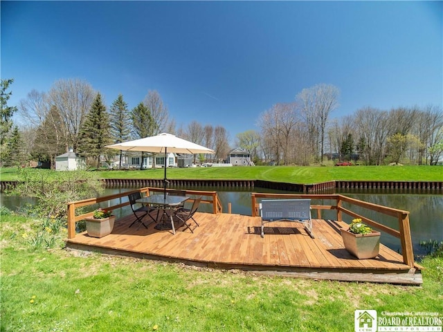 deck featuring a lawn, outdoor dining space, a water view, and a shed