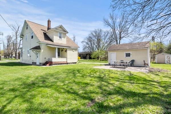 back of house featuring an outdoor structure, a lawn, a chimney, and a patio