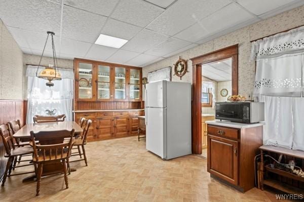 kitchen featuring brown cabinetry, black microwave, light countertops, freestanding refrigerator, and glass insert cabinets