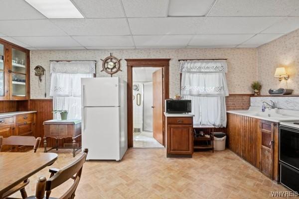 kitchen with freestanding refrigerator, a drop ceiling, brown cabinets, and black microwave