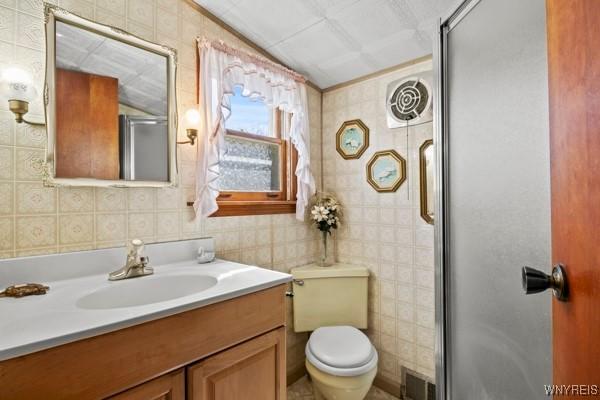 full bath with visible vents, tile walls, a stall shower, vanity, and toilet