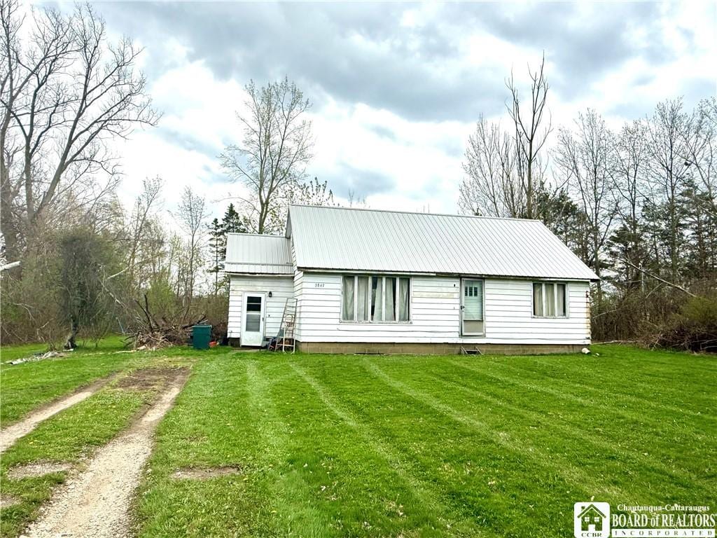 rear view of property featuring a yard, metal roof, and dirt driveway