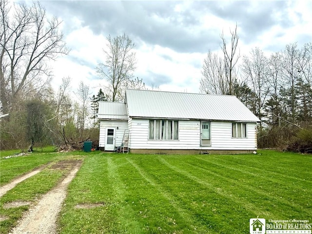 rear view of property featuring a yard, metal roof, and dirt driveway