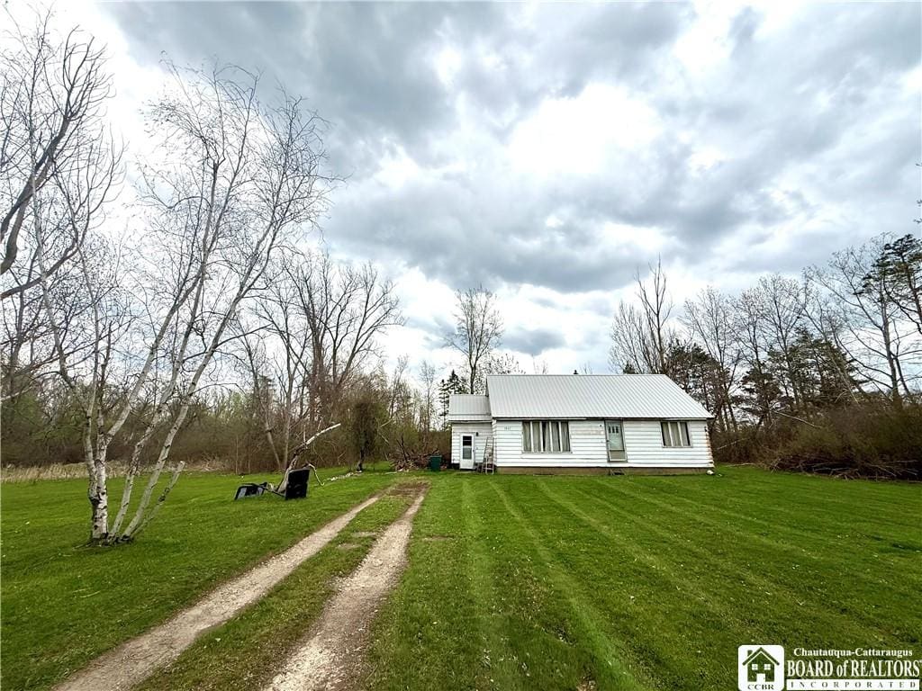 view of front facade featuring driveway, metal roof, and a front yard