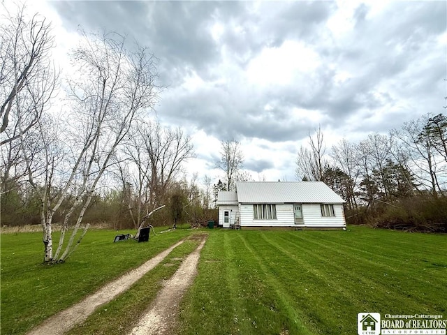 view of front facade featuring driveway, metal roof, and a front yard