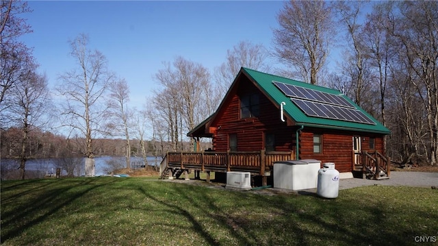 view of side of property featuring log siding, a deck with water view, roof mounted solar panels, a yard, and metal roof