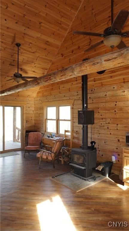 living area with a wood stove, wood walls, wood finished floors, high vaulted ceiling, and a ceiling fan