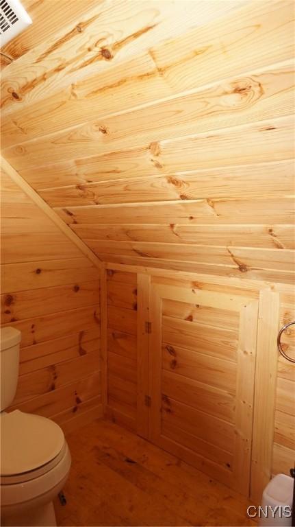 half bath featuring wood walls, wood finished floors, and toilet
