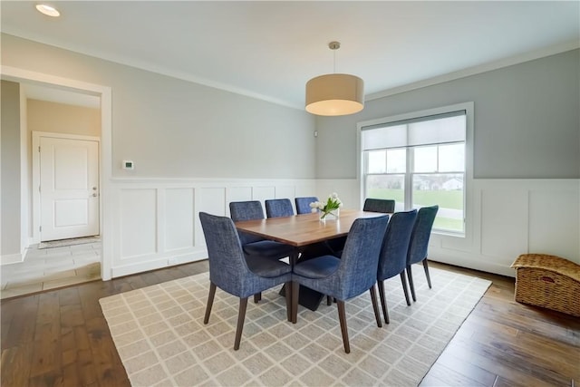 dining area featuring wainscoting, light wood-style flooring, and a decorative wall