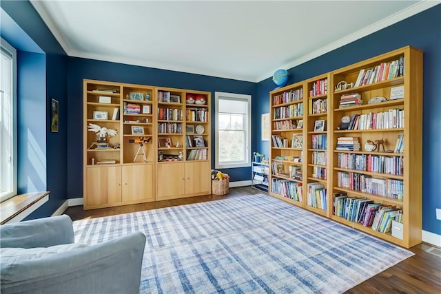 sitting room featuring crown molding, baseboards, bookshelves, and wood finished floors