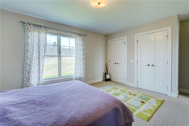 bedroom with baseboards, two closets, and light colored carpet