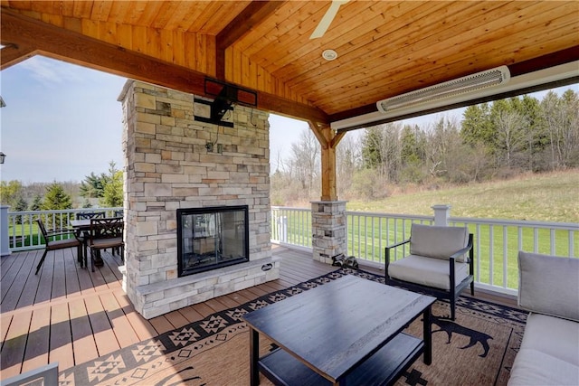 wooden deck with outdoor dining space, a yard, and an outdoor stone fireplace