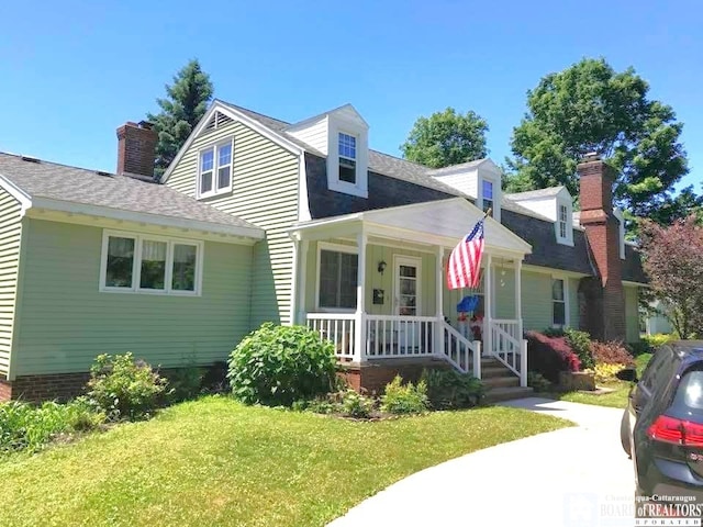 new england style home featuring covered porch, roof with shingles, and a front lawn